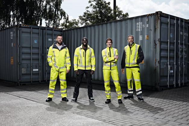 Drie mannen en een vrouw in neongeel beschermende kleding bevinden zich in een recyclingcentrum.